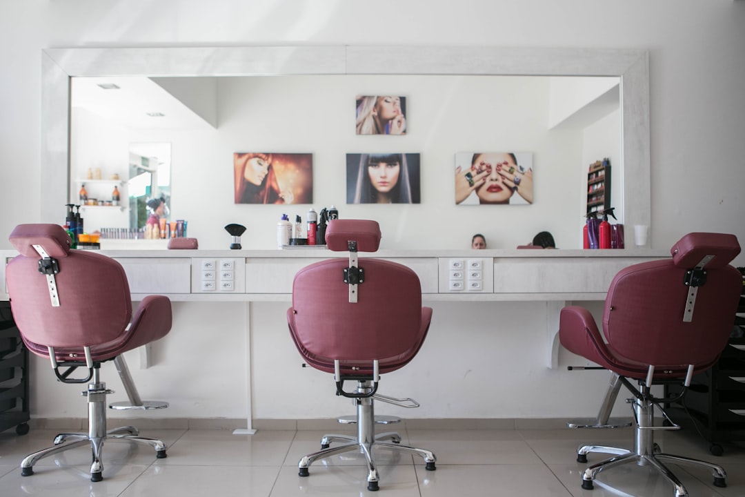 Three maroon salon chairs facing a long white counter with a large mirror